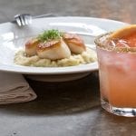 Grapefruit cocktail with seasoned rim and scallop dish in background