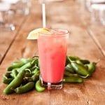 ruby red cocktail served with a lemon and staged with jalapeños on wood table