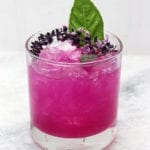 Bright pink dragon fruit cocktail with basil blossom and basil leaves