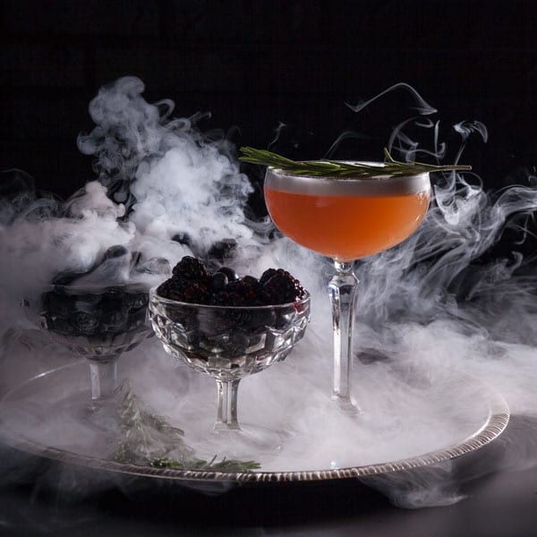 Orange cocktail for a Halloween shoot on a tray with two glasses filled with blackberries surrounded by smoke