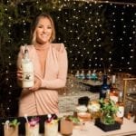 Becca Tilley with tiki cocktails behind a Snake Oil Cocktail Co bar holding a white mixer